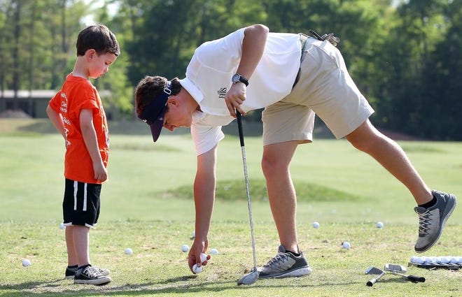 Avery Price, a former Forestview High School golfer, tees up a ball on the driving range for Wade Poplin during a past installment of the Sticks for Kids golf clinic at the Cramer Mountain Club. The next Sticks for Kids clinic will take place April 16, and registration for the 50 open slots will open March 18. [John Clark/The Gaston Gazette]