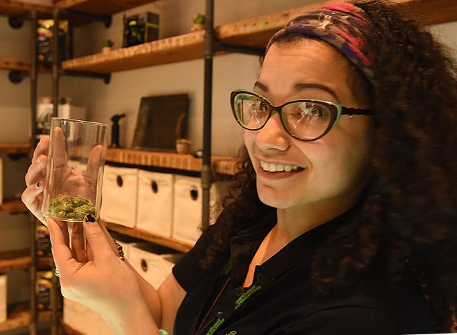Marisol Rosa holds up a container of cannabis flowers behind the counter at Northeast Alternatives on Monday in Fall River, Mass. [JACK FOLEY/HERALD NEWS PHOTO]