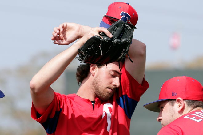 FILE - In this Feb. 19, 2019, file photo, Philadelphia Phillies starting pitcher Aaron Nola wipes his face at the Phillies spring training baseball facility, in Clearwater, Fla. It may look like a few weeks of relaxed fun in the sun, but make no mistake: Spring training can be a grind. Pitchers need to build their arms up slowly, and position players face their own challenges. At this time of year, Florida and Arizona are obviously better for baseball than many other American climates, but the warm, sunny weather does have a few drawbacks. (AP Photo/Lynne Sladky, File)