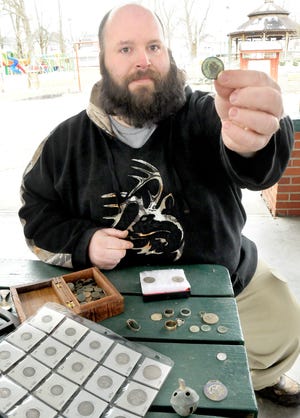 Byesville resident Will Sills holds up a very old rare coin he found recently while using a metal detector in the village. On the table is a collection of his finds.