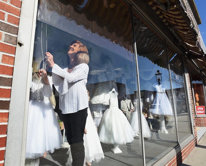 Nelly Silva lowers a transparent yellow curtain to shield the dresses in her display window from the harsh afternoon sunshine, in the store she's owned for four decades, Nelly's Boutique, seen Tuesday, March 12, 2019, in Fall River, Massachusetts. [Herald News Photo | Jack Foley]