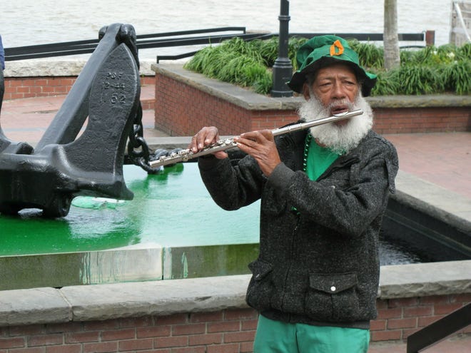 Marion May wears a leprechaun hat while playing his flute next to a fountain of green-dyed water on the downtown riverfront of Savannah, Georgia, on Wednesday, March 13, 2019. Savannah is gearing up for its 195-year-old St. Patrick's Day parade, the city's largest tourism event of the year. (AP Photo/Russ Bynum)