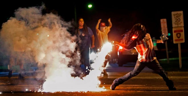 In this Aug. 13, 2014, file photo Edward Crawford Jr., returns a tear gas canister fired by police who were trying to disperse protesters in Ferguson, Mo. Six young men with connections to the Ferguson protests, including Crawford, have died, drawing attention on social media and speculation in the activist community that something sinister is at play. Police say there is no evidence the deaths have anything to do with the protests and note that only two were homicides. But activists and observers remain puzzled and wonder if they'll ever get answers. Crawford fatally shot himself in May 2017 after telling acquaintances he had been distraught over personal issues, police said.