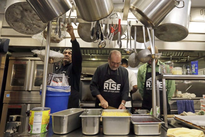 Lucas Almeida, left, and Ray Duarte, right, give Bishop Edgar M. da Cunha a hand cooking a meal using one of the Rice Bowl recipies at the Sister Rose House in New Bedford. [ PETER PEREIRA/THE STANDARD-TIMES ]