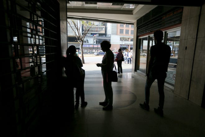 People wait inside a darkened office building during a power outage in Caracas, Venezuela, Monday, March 25, 2019. The subway suspended service because of the power cuts Monday, as local media reported outages in at least six states. (AP Photo/Fernando Llano)