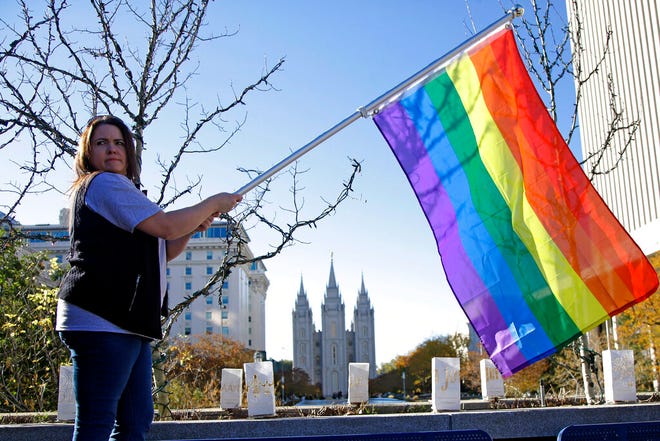FILE - In this Nov. 14, 2015 file photo, Sandy Newcomb poses for a photograph with a rainbow flag as people gather for a mass resignation from The Church of Jesus Christ of Latter-day Saints in Salt Lake City. The Church of Jesus Christ of Latter-day Saints is repealing rules unveiled in 2015 that banned baptisms for children of gay parents and made gay marriage a sin worthy of expulsion. The surprise announcement Thursday, April 4, 2019, by the faith widely known as the Mormon church reverses rules that triggered widespread condemations from LGBTQ members and their allies. (AP Photo/Rick Bowmer, File)