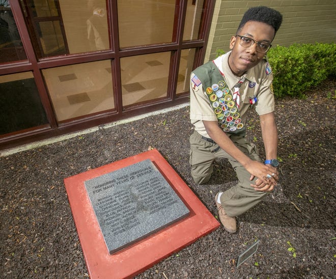 Eagle Scout Reggie Willis kneels next to the granite monument that bears the names of 21 teachers who worked at North Marion Middle School for at least 25 years or more. The endeavor was his community service project, which is a requirement to attain the rank of Eagle. Willis is a senior at West Port High School and plans to attend Florida A&M University after graduation. [Alan Youngblood/Ocala Star-Banner]