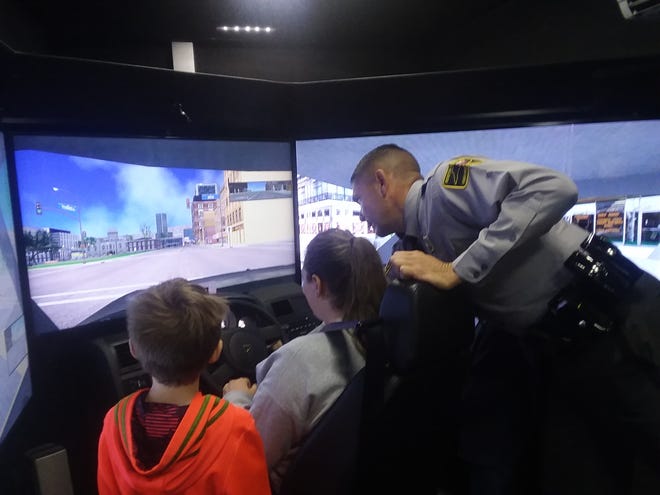 N.C. Highway Patrol trooper Eric Mellott instructs Joni Dudley, with her 8-year-old son Kaden on a traffic simulator. [RODGER MULLEN/THE FAYETTEVILLE OBSERVER]