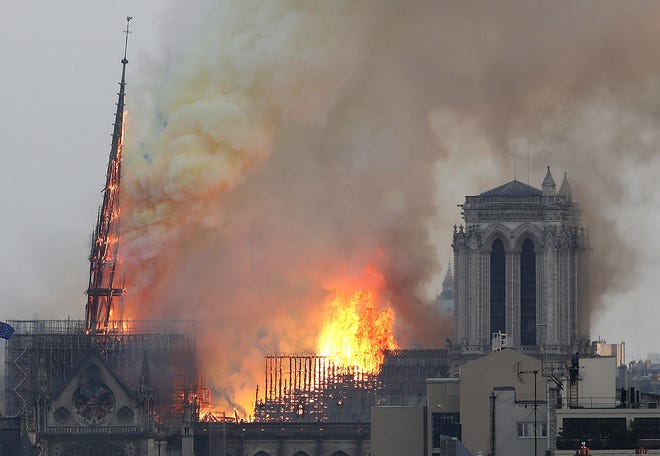 Flames rise from Notre Dame cathedral as it burns in Paris on Monday. Massive plumes of yellow brown smoke is filling the air above Notre Dame Cathedral and ash is falling on tourists and others around the island that marks the center of Paris. [Thibault Camus/The Associated Press]