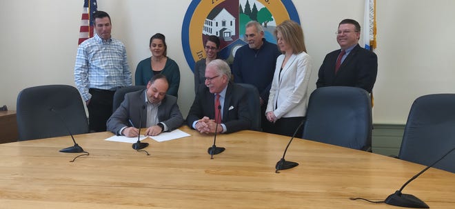 Ashland Town Manager Michael Herbert, with pen, and Needham Bank Executive Vice President Eric Morse sign a partnership agreement Thursday in Town Hall. Others attending include Economic Development Advisory Group members Dennis Ahern and Julia Chase, Assistant Town Manager Jennifer Ball, Selectman Steve Mitchell, Needham Bank Ashland branch manager Denise Loiselle and Needham Bank Vice President James Dietel.  [Daily News Photo / Cesareo Contreras]