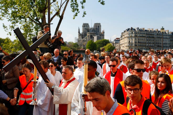 With Notre Dame cathedral in background, religious officials carry the cross during the Good Friday procession, Friday, April 19, 2019 in Paris. Top French art conservation officials say the works inside Notre Dame suffered no major damage in the fire that devastated the cathedral, and the pieces have been removed from the building for their protection.(AP Photo/Francois Mori)