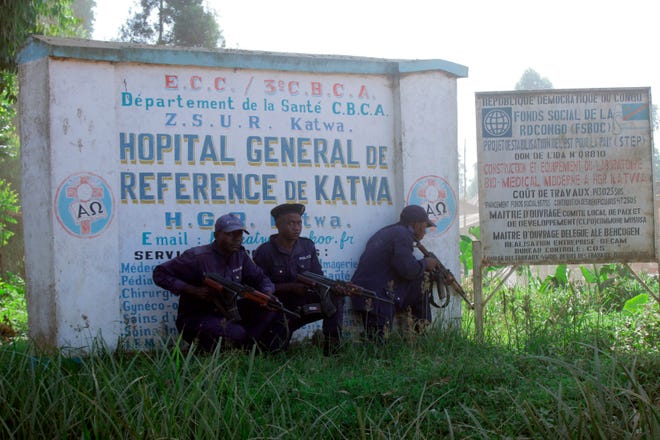 Police shelter behind a hospital sign, as they guard a hospital in Butembo, Congo, on Saturday after militia members attacked an Ebola treatment center in the city’s Katwa district overnight. Violence has deeply complicated efforts to contain what has become the second-deadliest Ebola virus outbreak in history. [Al-Hadji Kudra Maliro/The Associated Press]