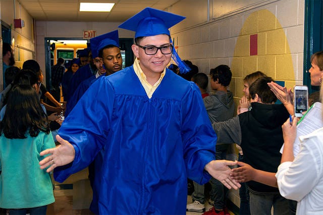 WAY TO GO! — Asheboro High School senior Juan Vega walks down the hallway of Donna Lee Loflin Elementary, his former school, in his cap and gown, giving high fives to current students. (Scott Pelkey / Special to The Courier-Tribune)