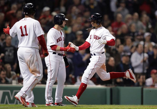 Boston Red Sox's Mookie Betts, right, is congratulated by Andrew Benintendi, center, after they both scored on a two RBI double by Xander Bogaerts off Oakland Athletics starting pitcher Frankie Montas during the third inning of a baseball game at Fenway Park, Monday, April 29, 2019, in Boston. At left is Boston Red Sox's Rafael Devers (11.(AP Photo/Charles Krupa)