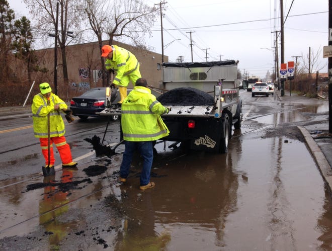 Published Caption:       The water having receded, workers fill the pothole.



 Original Caption: Workers fill a pothole on Allens Avenue, Providence, that caused several flat tires on Monday morning. [The Providence Journal/Sandor Bodo.]