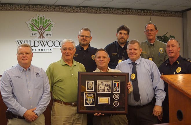 Representatives of the city of Wildwood and the Wildwood police department pose with the shadow box, Monday morning at the city com,mission meeting. Chief Randall Parmer is front right. Former chief Edward Reeser is front left. David Clarkson is holding the box, and mayor Ed Wolf is to his side, in a green shirt. [LINDA CHARLTON / CORRESPONDENT]