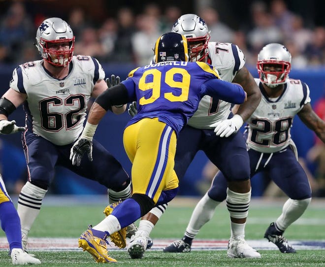 Offensive lineman #62 Joe Thuney and #77 Trent Brown along with running back #28 James White keep Rams defensive lineman #99 Aaron Donald in check and away from Tom Brady during a pass play.
