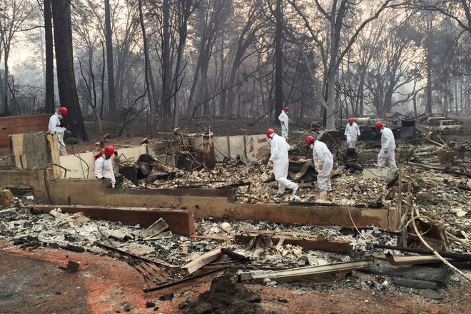 In this Nov. 15, 2018 file photo, volunteer rescue workers search for human remains in the rubble of homes burned in the Camp Fire in Paradise, Calif.