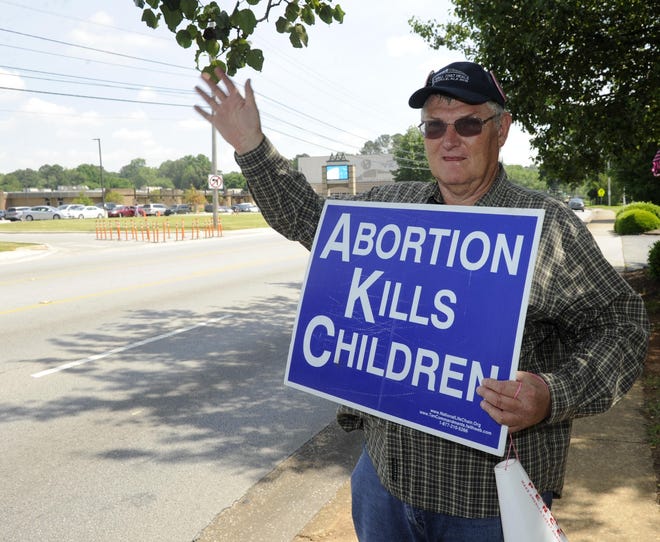 Jim Snively, of Huntsville, Alabama, waves to passing cars Friday while holding an anti-abortion sign in front of the Alabama Women's Wellness Center. [AP Photo/Eric Schultz]