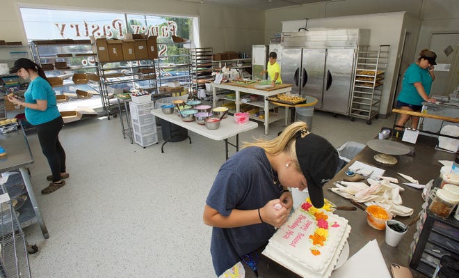 In the Fancy Pastry finishing kitchen, Haley Robertson (from left) puts icing on cupcakes, Mallory Mize decorates a cake, Julie Manuel applies icing to long johns and Michelle Hilliard takes a phone-in order. [Donnie Roberts/The Dispatch]