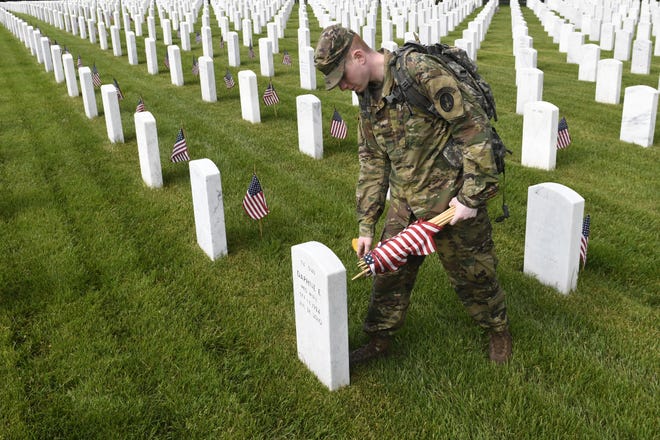 Cpl. Matthew Munie of Jackson, Mich., places a flag in front of a headstone at Arlington National Cemetery in Arlington, Va., Thursday, May 23, 2019. [AP Photo/Susan Walsh]