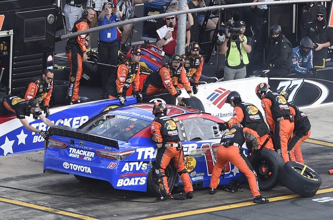 Crew members lift Martin Truex Jr.'s car to change a flat tire during a NASCAR Cup Series race Sunday night at Charlotte Motor Speedway in Concord, N.C. [MIKE MCCARN/THE ASSOCIATED PRESS]