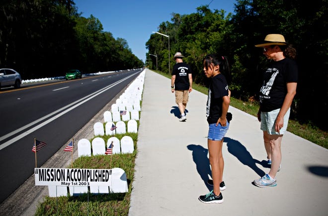 In this 2017 photo, volunteers walk down the Memorial Mile display set up by Gainesville Veterans for Peace along a stretch of Northwest Eighth Avenue in Gainesville. [The Gainesville Sun, File]