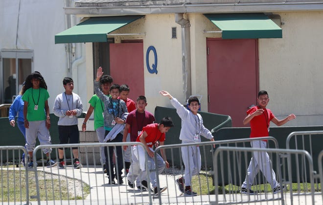 Migrant children wave to demonstrators calling to them across the street from the Homestead Temporary Shelter for Unaccompanied Children on April 19. [AP Photo/Wilfredo Lee, File]