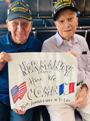 Gene Neeley, left, and Dale Bonney hold a sign as they prepare to leave the country for France to commemorate the 75th anniversary of the D-Day landings in Normandy, France. They are joining likely dozens of veterans from that war in France for the anniversary. [photo supplied by Phyllis Piraino]