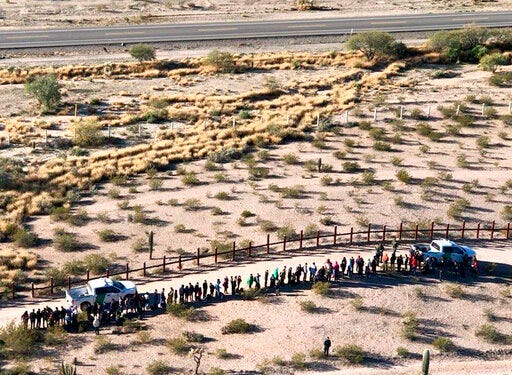 File - In this Thursday, Feb. 7, 2019, file aerial image released by the U.S. Customs and Border Protection, migrants, apprehended after illegally crossing along the U.S.-Mexico border near Lukeville, Ariz., are lined up. Mexico is at the top of the image, beyond the border fence. A border activist charged with helping a pair of migrants with water, food and lodging is set to go on trial in U.S. court in Arizona. Defendant Scott Daniel Warren has argued that his spiritual values compel him to help all people in distress. The trial is scheduled to begin Wednesday, May 29, 2019, in Tucson, with the 36-year-old Warren charged with harboring migrants and conspiring to transport and harbor two Mexican men found with him who were in the U.S. illegally. (U.S. Customs and Border Protection via AP, File)
