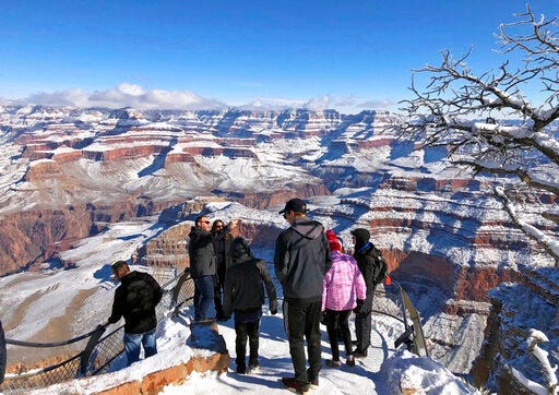 FILE - In this Jan. 1, 2019 file photo, tourists look at and take photos of a snow-covered Grand Canyon, in Arizona. A new report from the National Park Service says areas surrounding the Grand Canyon benefited last year from millions of tourism dollars. Grand Canyon National Park officials say the report found the 6.3 million people who visited in 2018 spent $947 million in communities near the park. (AP Photo/Anna Johnson, File)
