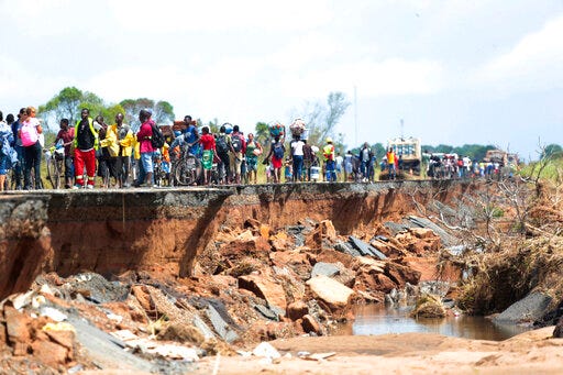FILE - In this Friday, March 22, 2019, file photo people pass through a section of the road damaged by Cyclone Idai in Nhamatanda about 50 kilometres from Beira, in Mozambique. Mozambique says it needs $3.2.billion to recover from two powerful tropical cyclones that ripped into the southern African nation this year and left hundreds dead. (AP Photo/Tsvangirayi Mukwazhi, File)