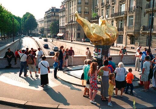 FILE - In this Thursday, Aug. 31, 2000 file photo, people gather around the gilded statue modeled on the flame of the Statue of Liberty that serves as an unofficial shrine to Princess Diana above the traffic tunnel where she died three years ago in Paris. Paris City Hall wants to name a small plaza after Princess Diana, at the site of the 1997 car crash that killed the cherished British royal. The site already holds a golden flame-shaped monument in her honor, adjacent to the Alma Tunnel where the accident occurred. (AP Photo/William Alix, File)
