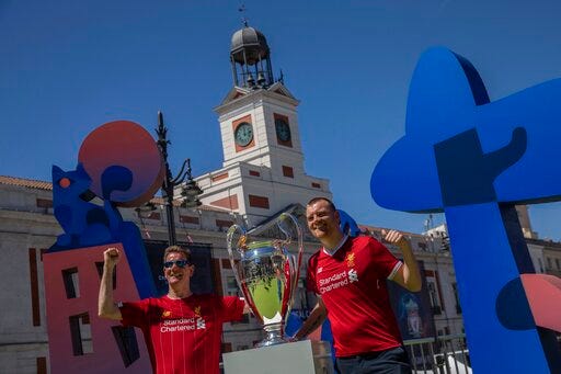 Liverpool supporters pose for a photo next to the Champions League trophy at Puerta del Sol square in downtown Madrid, Spain, Thursday, May 30, 2019. Liverpool and Tottenham were each allocated nearly 17,000 tickets for their fans, but Spanish authorities expect many thousands more to make the trip without tickets or pre-arranged lodging, heightening the possibility of fan trouble around the city. (AP Photo/Bernat Armangue)