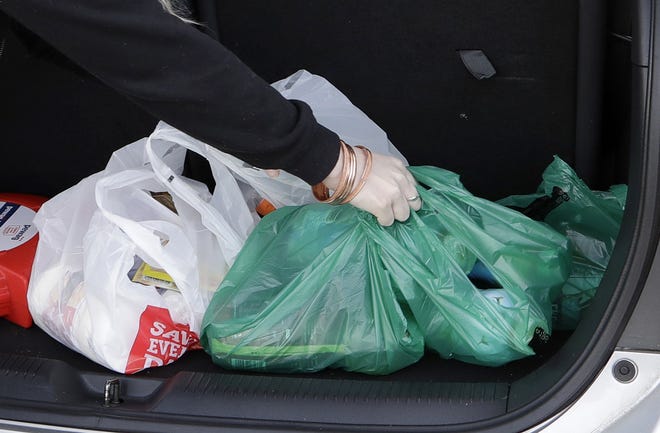 A shopper places goods in plastic bags into a car outside a supermarket. [Mark Baker/The Associated Press/File]
