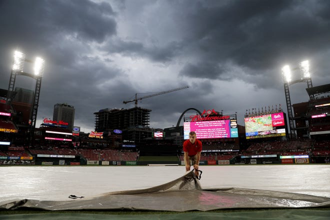Busch Stadium grounds crew member Lucas Hackmann helps pull a tarp over the field just prior to the scheduled start of a baseball game between the St. Louis Cardinals and the Cincinnati Reds on Wednesday in St. Louis. [Jeff Roberson/The Associated Press]