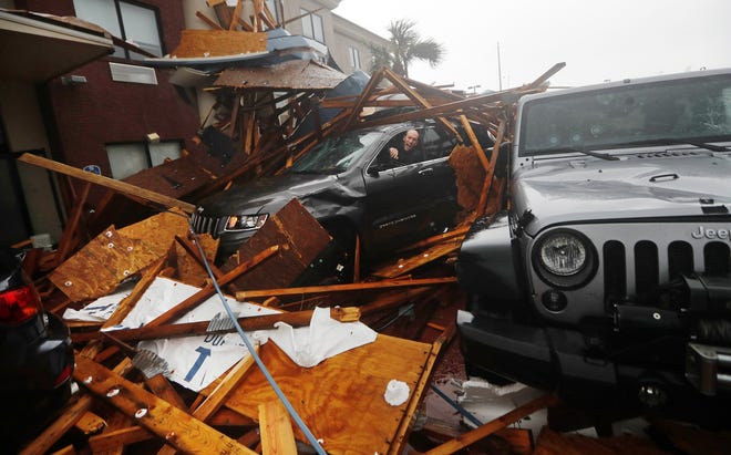In this Oct. 10, 2018, file photo, a storm chaser climbs into his vehicle to retrieve equipment after a hotel canopy collapsed, as the eye of Hurricane Michael passes over Panama City Beach. For some communities, the devastation remains an open wound, as in Florida's Panama City, slammed by Hurricane Michael last year. [AP Photo/Gerald Herbert]