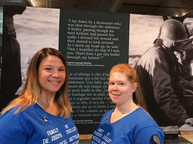 Tara Shelley and Shelley Walters stand in the Normandy visitors center at the American cemetery at Omaha Beach on Wednesday in front of a quote by their grandfather, former St. Augustine Mayor Joseph Shelley. [CONTRIBUTED]