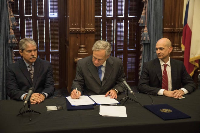 Gov. Greg Abbott signs into law House Bill 18, which improves mental health services for schools, at the Texas State Capitol Governor's Public Reception Room in Austin on Thursday. Seated on the left is Sen. Larry Taylor, R-Friendswood, and on the right, Rep. Greg Bonnen, R-Friendswood. [LOLA GOMEZ/AMERICAN-STATESMAN]