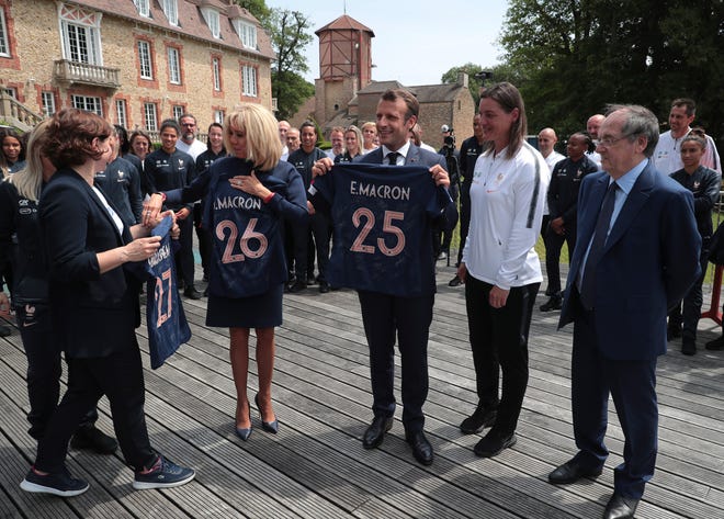 French President Emmanuel Macron, center, poses with a French National Women's Soccer team's jersey next to France's head coach Corinne Diacre, second right, his wife Brigitte Macron, second left, and head of the French Soccer Federation Noel le Graet, right, during a visit at France's training camp in Clairefontaine, south of Paris, France, Tuesday, June 4 2019. The French women soccer team is preparing for the FIFA Women's World Cup that will start in France next Friday. (Christophe Petit Tesson, Pool via AP)