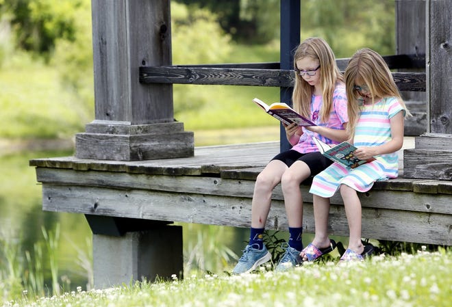 Aayca Mizer 9 and her sister Reese Mizer 6 (right) find a quiet spot to read across from the Hillard Branch Library. They were at the library with their grandmother Virginia Wittkugle and are enrolled in the summer reading program and had been at the library getting new books June 6, 2019. [Eric Albrecht/Dispatch]