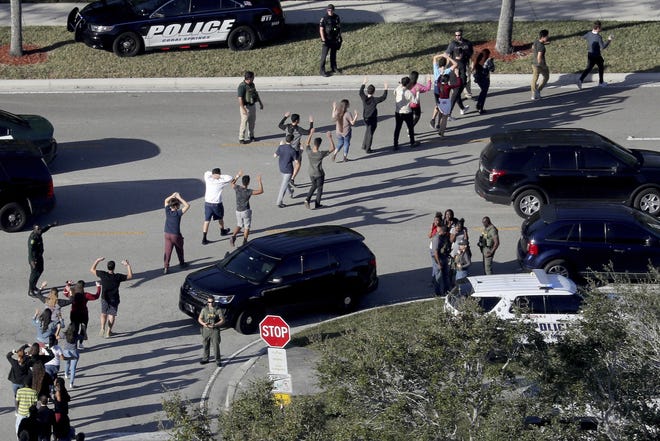 Students hold their hands in the air as they are evacuated by police from Marjory Stoneman Douglas High School in Parkland on Feb. 14, 2018, after a shooter opened fire on the campus. [Mike Stocker/South Florida Sun-Sentinel via AP]