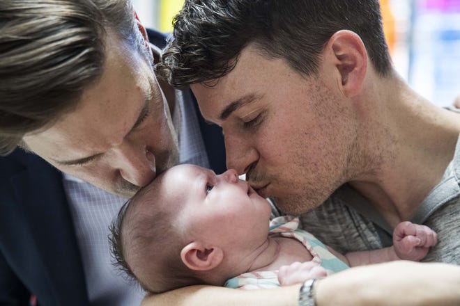 Austin City Manager Spencer Cronk, left, and his husband, Brendan Bujold, kiss their newborn daughter, Lauren, at the Austin Central Library in early June. [LOLA GOMEZ / AMERICAN-STATESMAN]