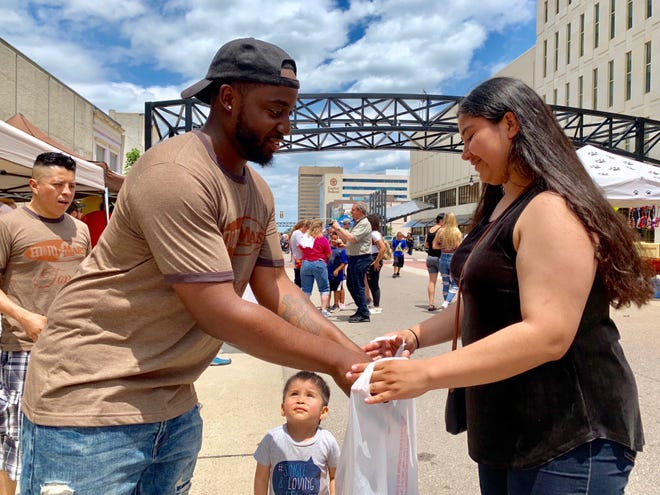 Mars employee Michael Kyles, left, puts a handful of chocolate candy in a bag held by Esmeralda Gonzalez, 16, as her 2-year-old nephew Rafael Herrada looks on during Saturday's Chocolae Festival in downtown Topeka. [Phil Anderson/The Capital-Journal]