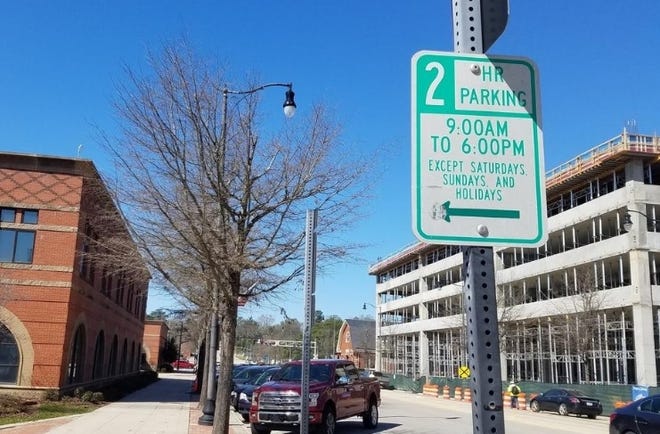 A parking sign near the Fayetteville Police headquarters downtown, with a new parking deck under construction in the background. The city is looking to expand pay parking downtown; business owners are organizing in opposition. [File/The Fayetteville Observer]