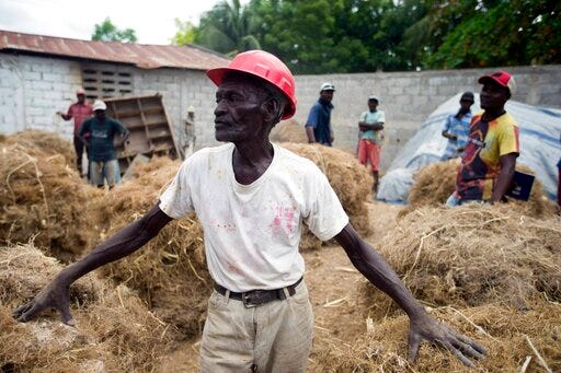In this May 27, 2019 photo, Clerme Elmacide stands amid bales of vetiver roots at a plant in Les Cayes, Haiti. In the poorest country of the Western hemisphere, this is ground zero for a multimillion-dollar industry responsible for more than half the world's vetiver oil, an essential oil used in fine perfumes ranging from Chanel to Guerlain. (AP Photo/Dieu Nalio Chery)