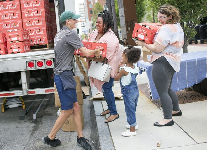 Noah Harper hands a box of peaches to Cameron Lindsey while her daughter Callen, 4, and Mikayla Krell look on during The Peach Truck Tour stop at John F. Wolfe Columbus Commons on Friday. [Brooke LaValley/Dispatch]