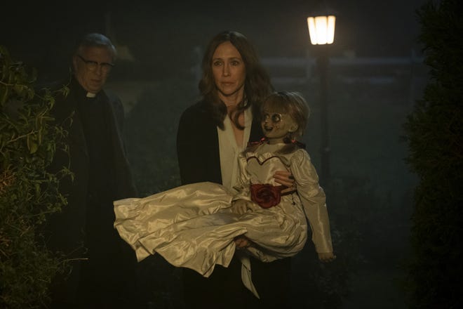 Vera Farmiga, right, carries the titular devil-doll in "Annabelle Comes Home," as Steve Coulter, left, playing a priest, prepares to sprinkle the cursed toy with holy water. [JUSTIN LUBIN/WARNER BROS. PICTURES]