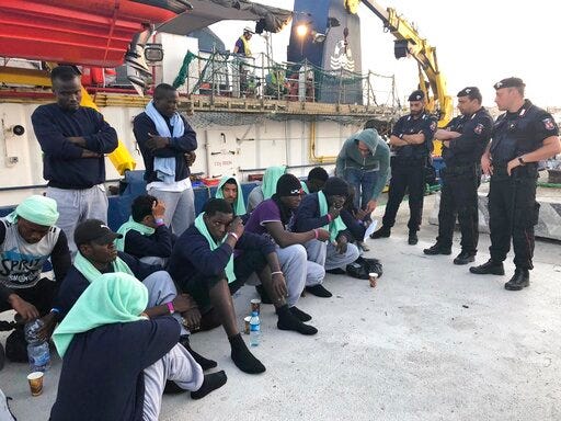 Migrants sit on the quay after disembarking at Lampedusa harbor, Italy, Saturday, June 29, 2019. Forty migrants have disembarked on a tiny Italian island after the captain of the German aid ship which rescued them docked without permission. Sea-Watch 3 rammed an Italian border police motorboat as it steered toward the pier on Lampedusa. (AP Photo/Annalisa Camilli)