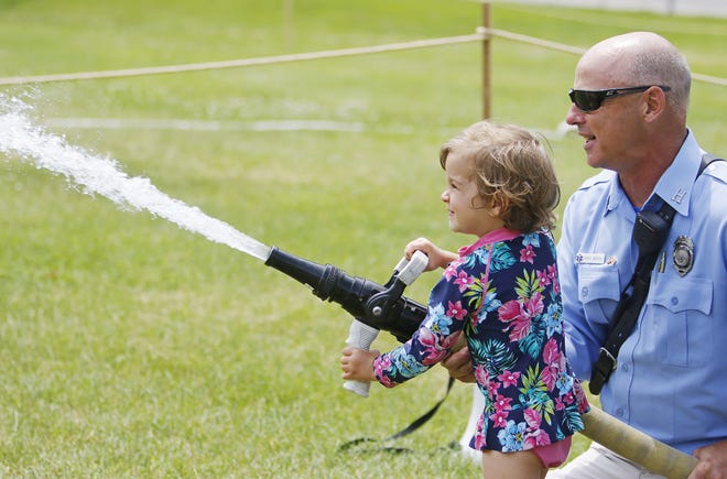 Sophia Bearce, 3, of Waterville, Maine, aims water at a target with a fire hose with help from Capt. Gary Woods at the York Beach Fire Department Muster on Sunday. [Jill Brady/Seacoastonline]